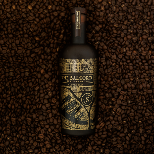 Salford Coffee Rum 70cl bottle laying on a bed of roasted coffee beans showing the gold map design.